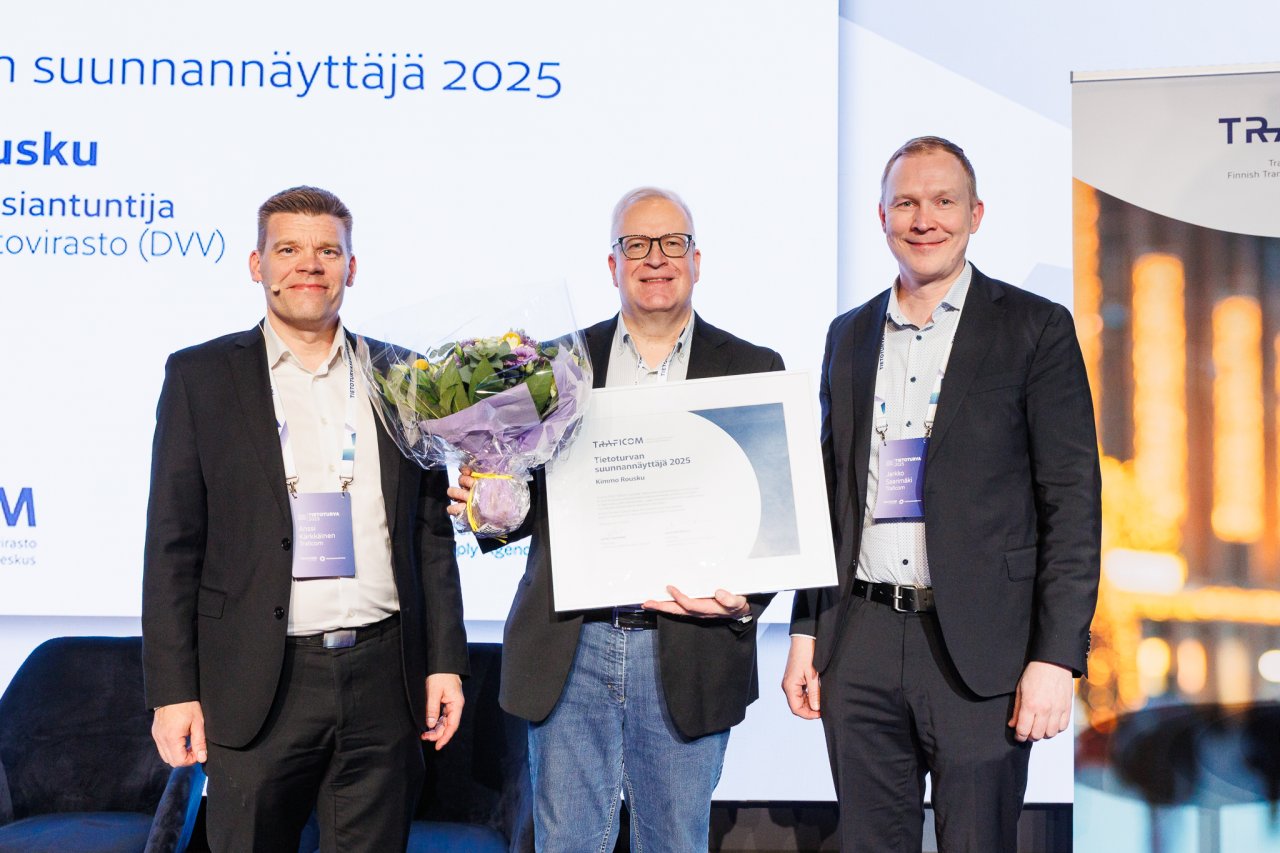 Traficomin Kyberturvallisuuskeskuksen ylijohtaja Anssi Kärkkäinen ja Traficomin pääjohtaja Jarkko Saarimäki onnittelevat Tietoturvan suunnannäyttäjä-diplomia ja kukkakimppua pitelevää Kimmo Rouskua