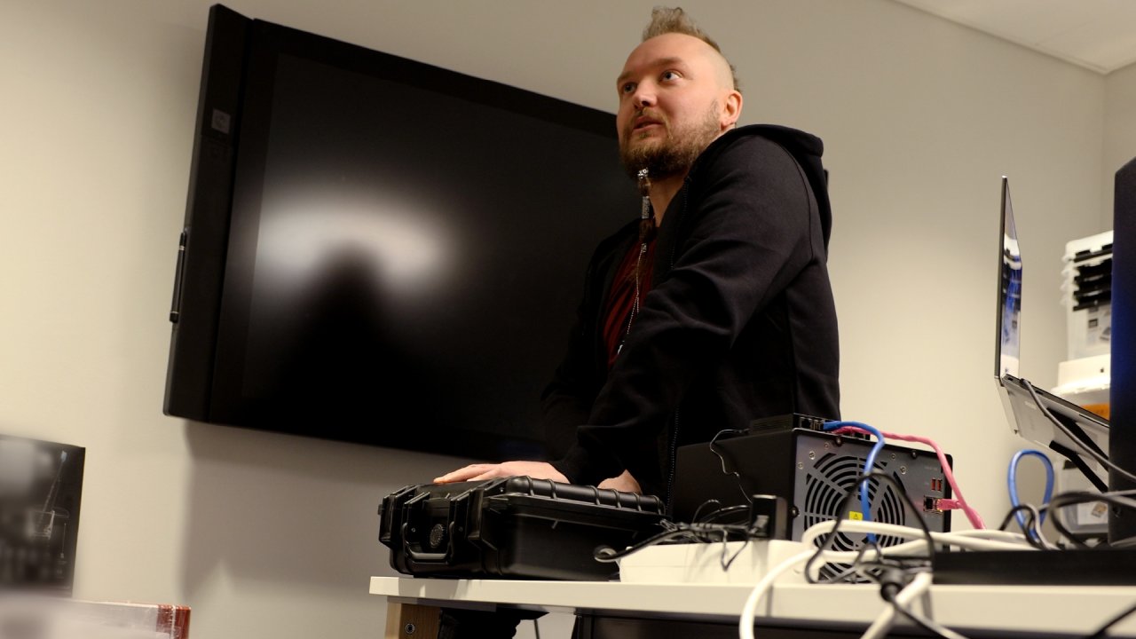 Eritysiasiantuntija Heikki Juva istuu työhuoneensa pöydällä, älylaittepakkausten ja hakkerointivälineiden ympäröimänä.