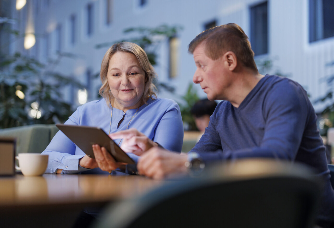 Kaksi henkilöä tarkastelee tablettia ja keskustelee digitaalisesta sisällöstä toimistotilassa.
